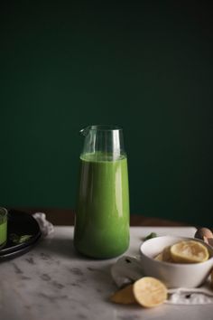 a pitcher filled with green liquid sitting on top of a table next to lemon slices