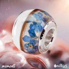 a blue and white flowered glass bead on top of some pink rocks with water droplets