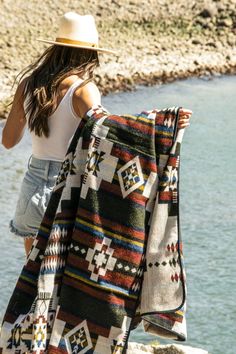 a woman is standing by the water with a blanket on her shoulders and hat on