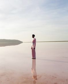 a woman standing on top of a beach next to a body of water in the distance