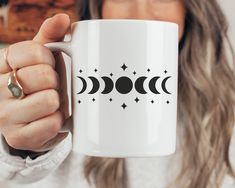 a woman is holding a coffee mug with the moon and stars on it in front of her face