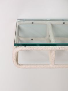 a white table with glass top and metal frame on the bottom, against a white wall