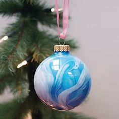 a blue and white ornament hanging from a christmas tree with a pink ribbon