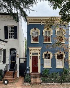 a blue house with white trim and red door on the street in front of other houses