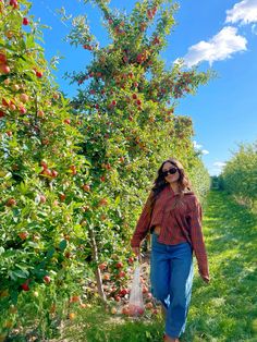 a woman is walking through an apple orchard