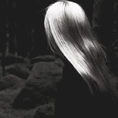 a woman with long white hair standing in front of some rocks and looking into the distance