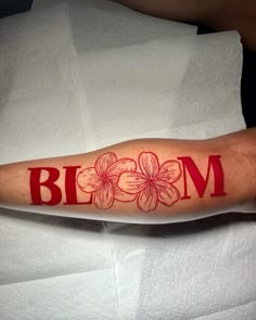 a person with a red ink tattoo on their arm and the word bloom written in it