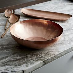 two copper colored bowls on a marble counter top with spoons and utensils