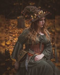 a woman wearing a green dress and hat sitting in the woods with leaves on her head