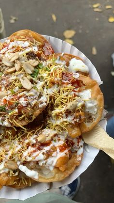 a person holding a pizza with toppings on it in a paper plate and wooden spoon