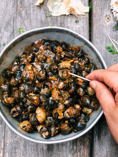 a person holding a spoon in a bowl full of mussels on a wooden table