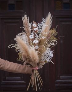 a woman holding a bouquet of dried flowers in front of a wooden door with snow on it