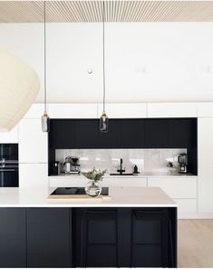 a kitchen with black cabinets and white countertops, an island in the middle is surrounded by hanging lights