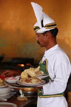 a man in white uniform holding a plate with food on it and another person standing next to him