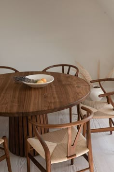 a wooden table with four chairs and a bowl of fruit on the plate in front of it