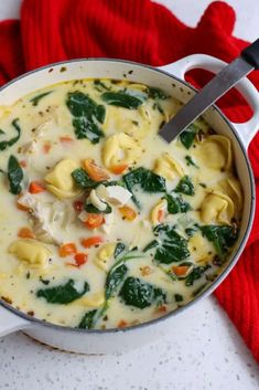 a pot filled with pasta and spinach on top of a white counter next to a red towel