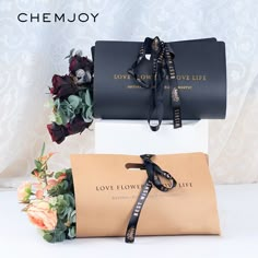 two black boxes with flowers in them on a white surface and one has a ribbon tied around it