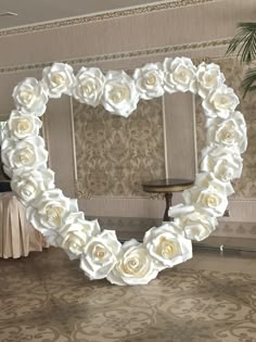 a heart shaped mirror with white roses on it in the middle of a room next to a table