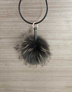 a black leather necklace with a fur ball hanging from it's center loop on a wooden surface