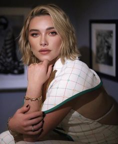 a woman with blonde hair wearing a white shirt and gold bracelet sitting on top of a bed