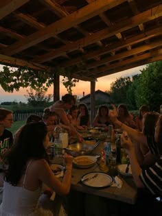 a group of people sitting around a wooden table eating food at sunset or dawn time