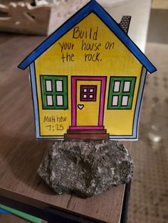 a paper house with the words build your house on the rock next to it is sitting on a table