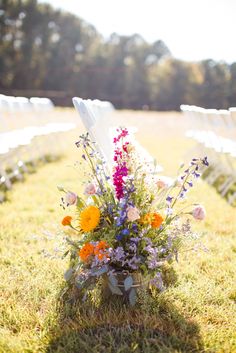 an arrangement of flowers sits in the grass near rows of white chairs