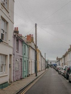 an empty street lined with parked cars in front of multi - colored buildings on a cloudy day