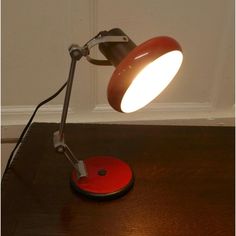 a red table lamp sitting on top of a wooden desk