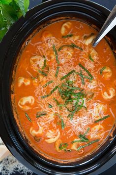 a crock pot filled with tortellini and tomato soup, garnished with parmesan cheese