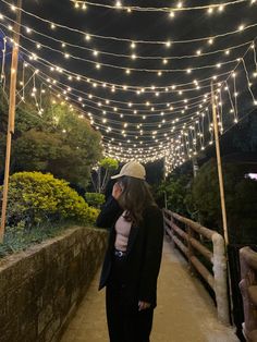 a woman standing on a bridge with lights strung over her head