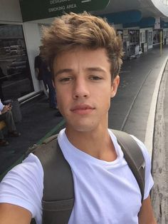 a young man is taking a selfie in front of a train station while wearing a backpack