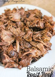 a white plate topped with sliced beef on top of a wooden table next to a fork and knife