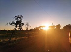 the sun is setting over an open field with a car parked in front of it