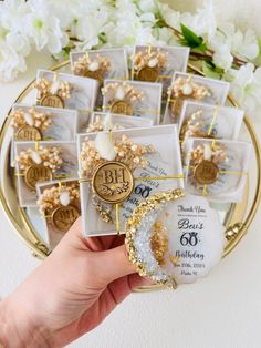 a hand holding a bunch of small white and gold tags in front of some flowers