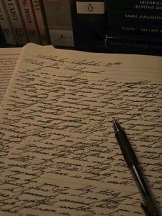 an open book with writing on it next to a pen and some books in the background