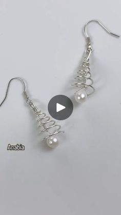 a pair of silver earrings with pearls hanging from the end of each earring, on a white background