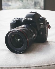 a canon camera sitting on top of a bed next to a window with the lens up