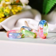 three different colored rings sitting on top of a white surface next to yellow and green flowers