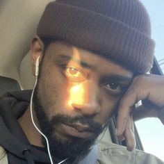 a man wearing headphones and a beanie looks at the camera while sitting in a car