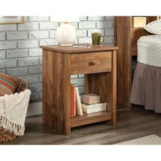 a wooden nightstand with books on it next to a brick wall and a bed in the background