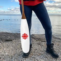 a woman holding a red paddle on the beach with ducks in the water behind her