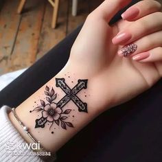 a woman's arm with a cross tattoo on it and flowers around the wrist