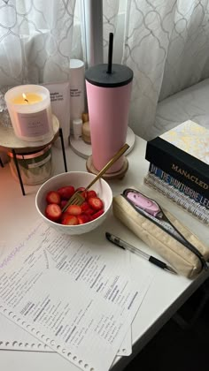 a bowl of strawberries sits on a table next to some books and a candle