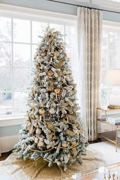 a decorated christmas tree in the corner of a living room with large windows and curtains