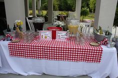 a red and white checkered table cloth with wine glasses on it is set up for an outdoor party