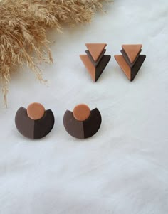 three pairs of earrings sitting on top of a white table next to some dried grass