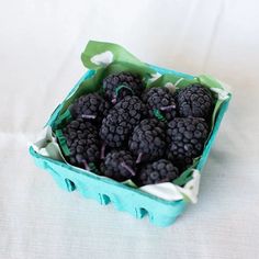 a blue basket filled with blackberries on top of a white table