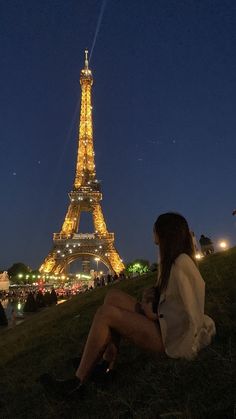 a woman sitting in front of the eiffel tower at night