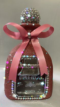 a bottle with a pink ribbon around it and some jewels on the top that are attached to it